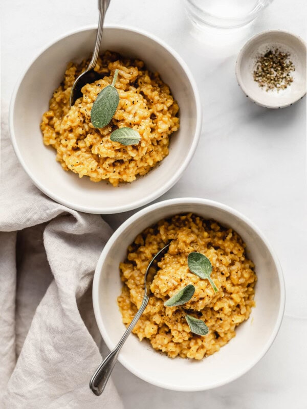 Two white bowls with risotto with butternut squash in them with a napkin on the side