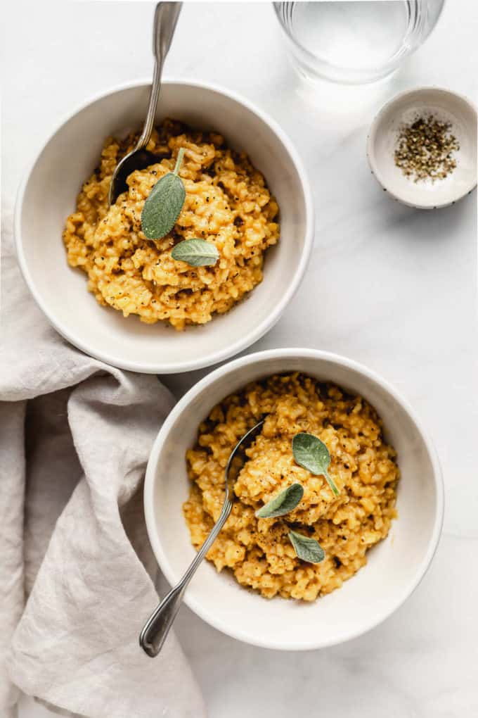Two white bowls with risotto with butternut squash in them with a napkin on the side