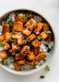 A bowl filled with rice and sweet and sour tofu topped with sliced green onions