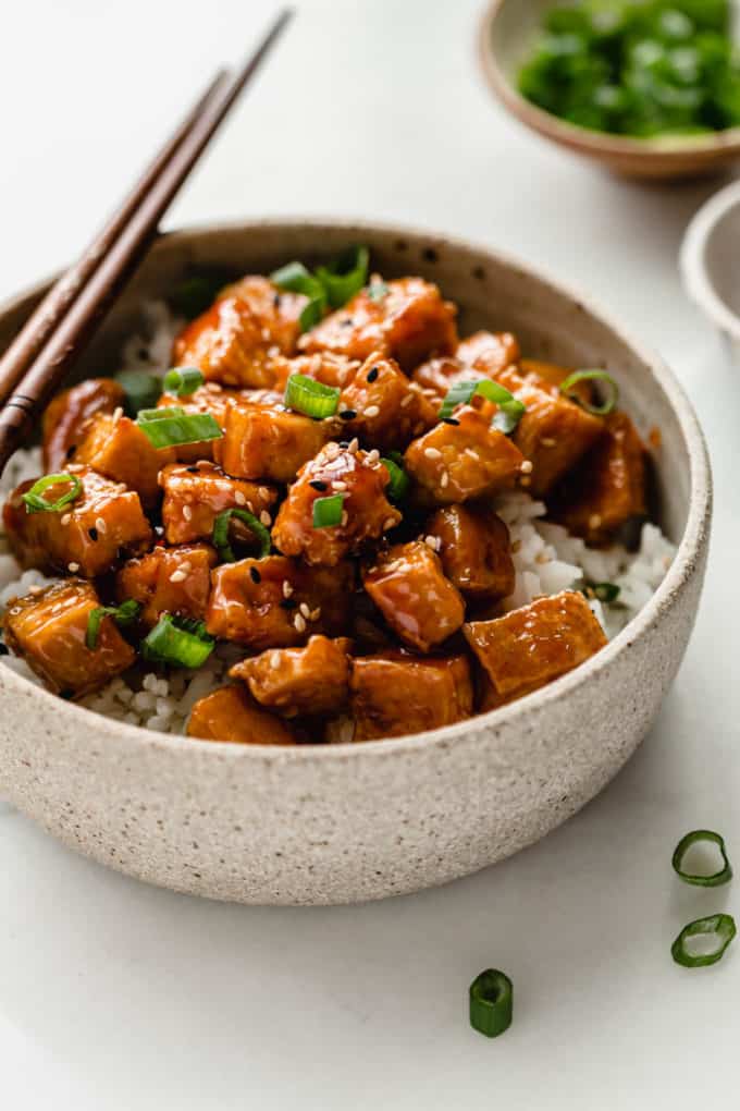 A ceramic bowl with asian tofu in it with a small bowl of green onions in the back