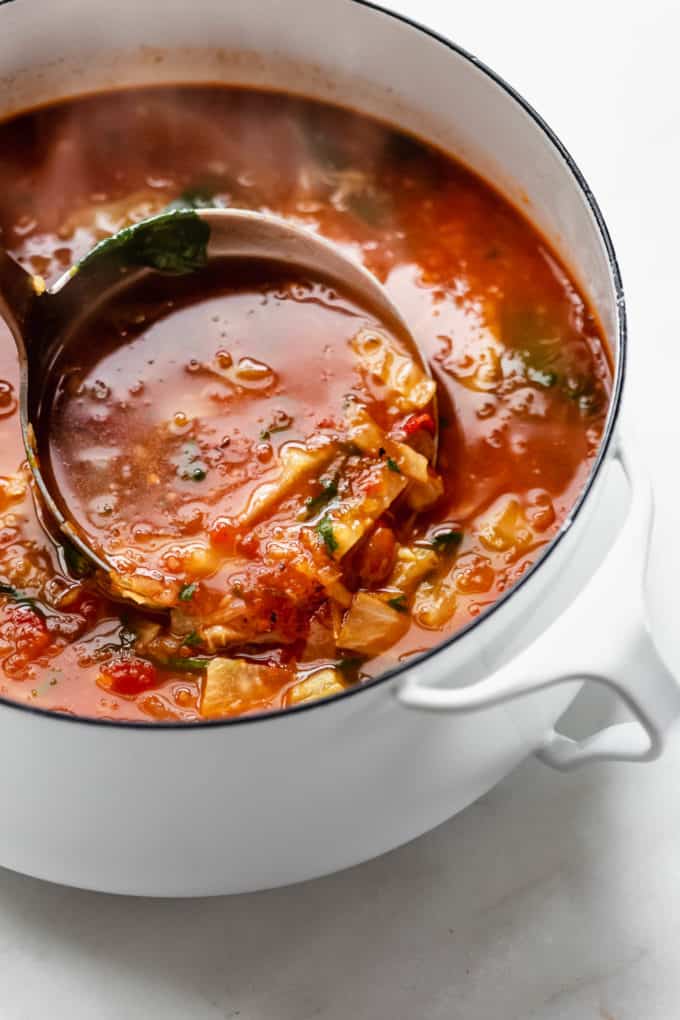 A Ladle scooping cabbage soup out of a white pot
