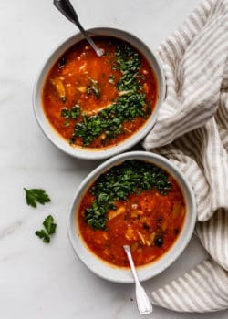 Two bowls of cabbage soup topped with parsley and a striped beige napkin on the side