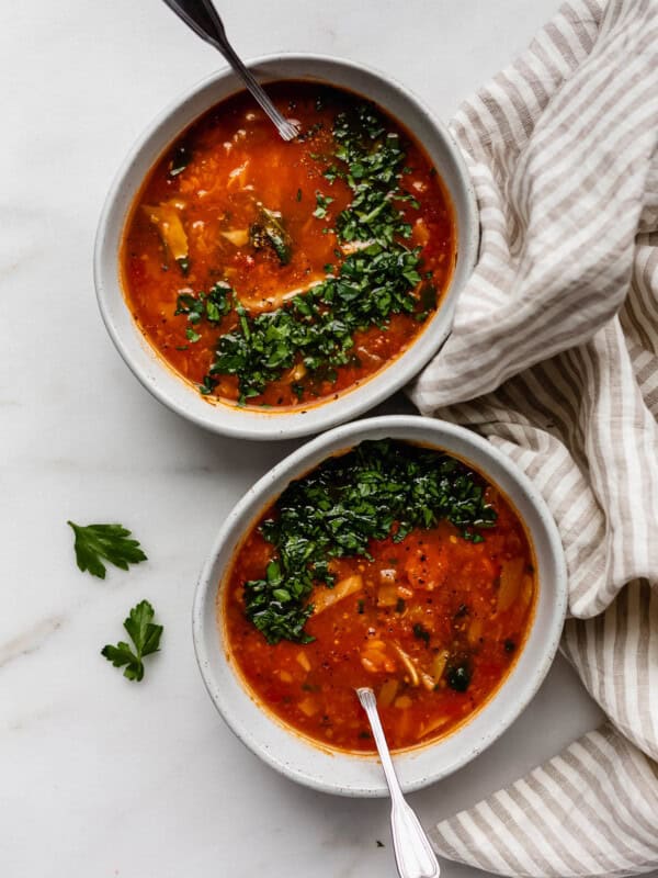 Two bowls of cabbage soup topped with parsley and a striped beige napkin on the side