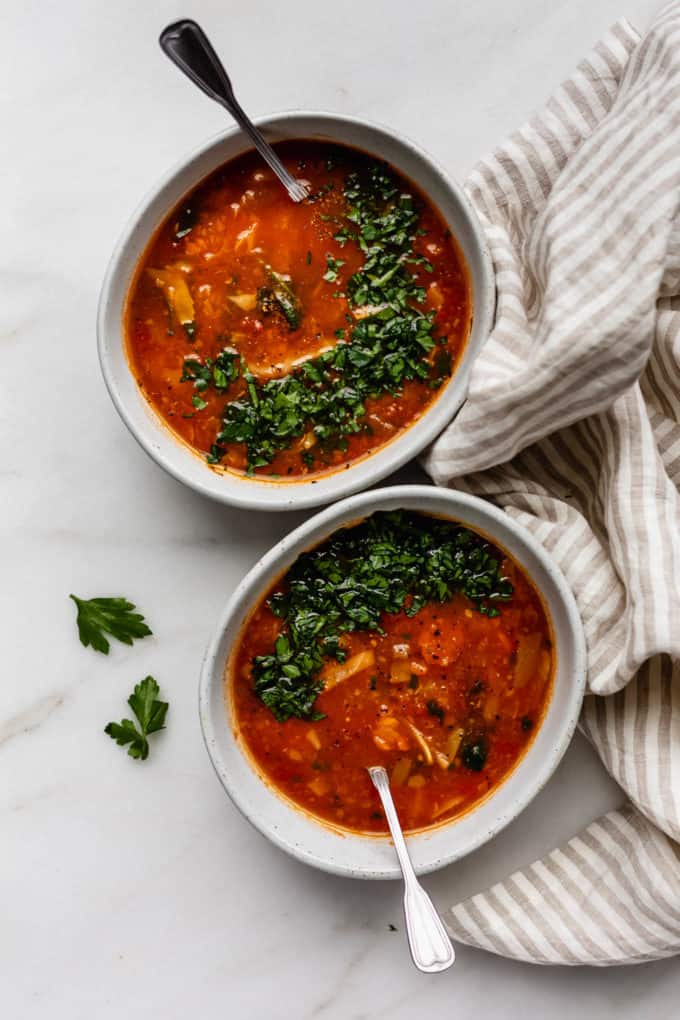 Two bowls of cabbage soup topped with parsley and a striped beige napkin on the side