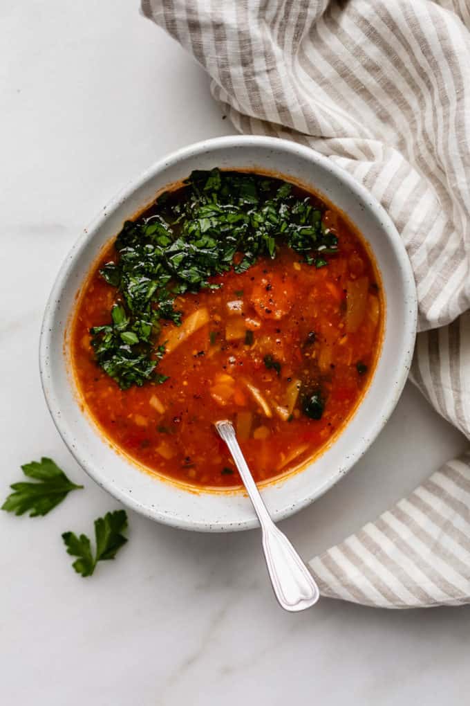 A bowl of cabbage soup topped with parsley and a spoon in it