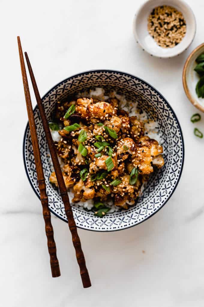 roasted cauliflower in a blue bowl topped with green onions and wood chopsticks