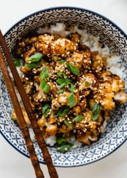 roasted cauliflower with sauce topped with green onions in a blue bowl