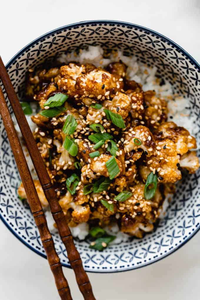 roasted cauliflower with sauce topped with green onions in a blue bowl