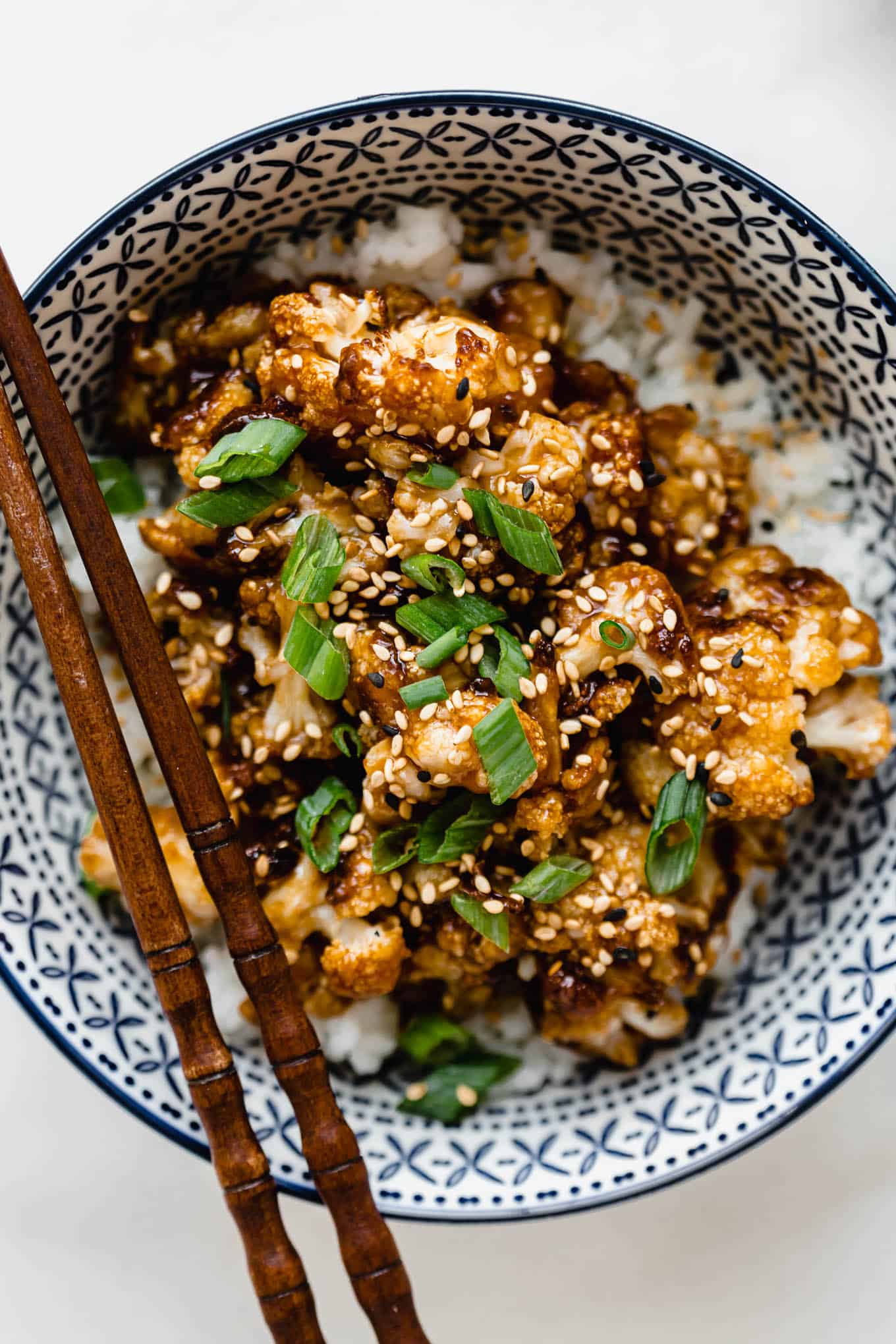 roasted cauliflower with sauce topped with green onions in a blue bowl