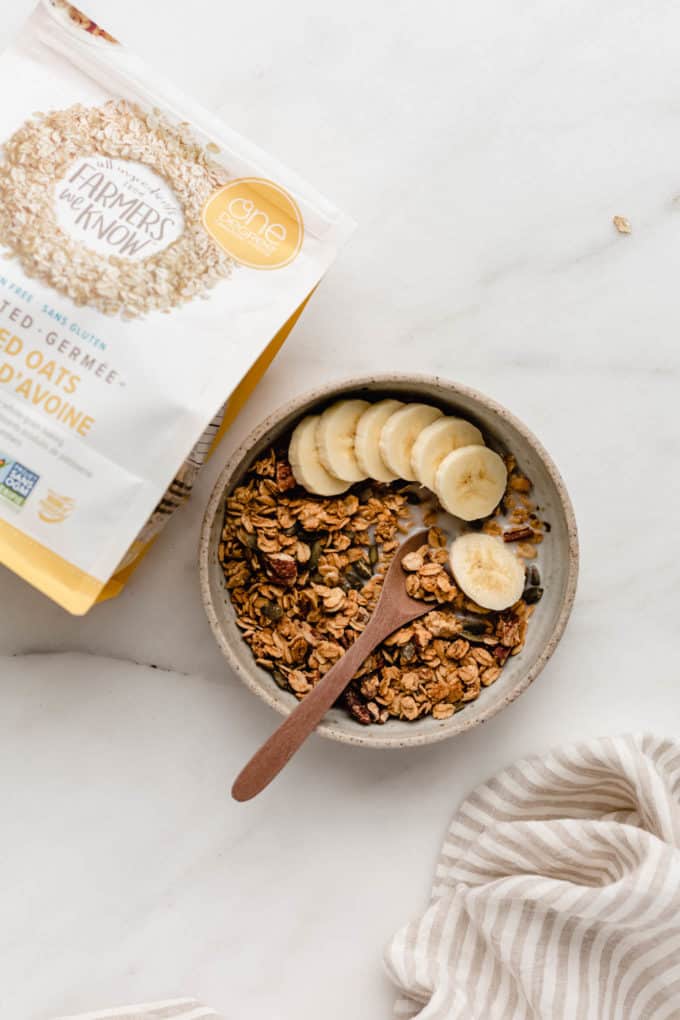A bowl of granola with bananas in it and a package of oats on the side
