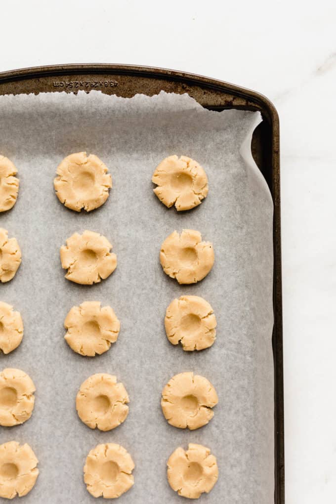 thumbprint cookies before being filled with jam on a baking sheet