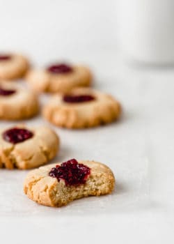 A vegan raspberry thumbprint cookie with a bite taken out of it on a marble counter