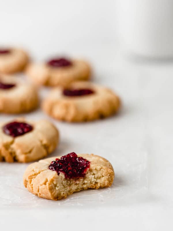 A vegan raspberry thumbprint cookie with a bite taken out of it on a marble counter