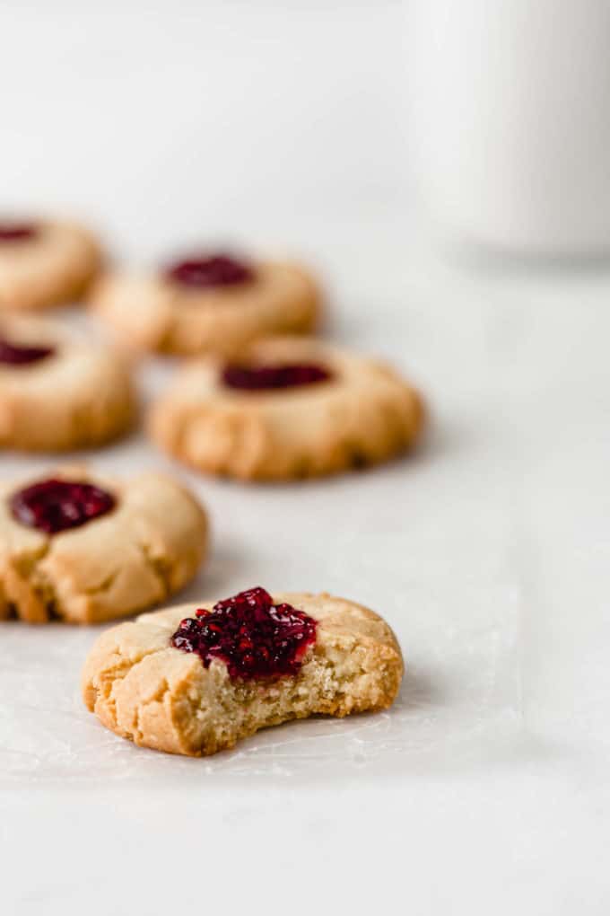 A vegan raspberry thumbprint cookie with a bite taken out of it on a marble counter