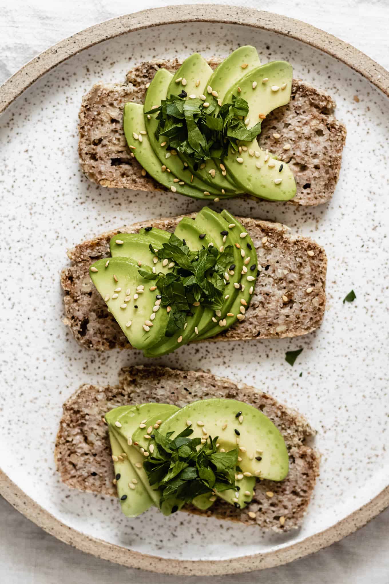 three slices of avocado toast on buckwheat bread on a white ceramic plate