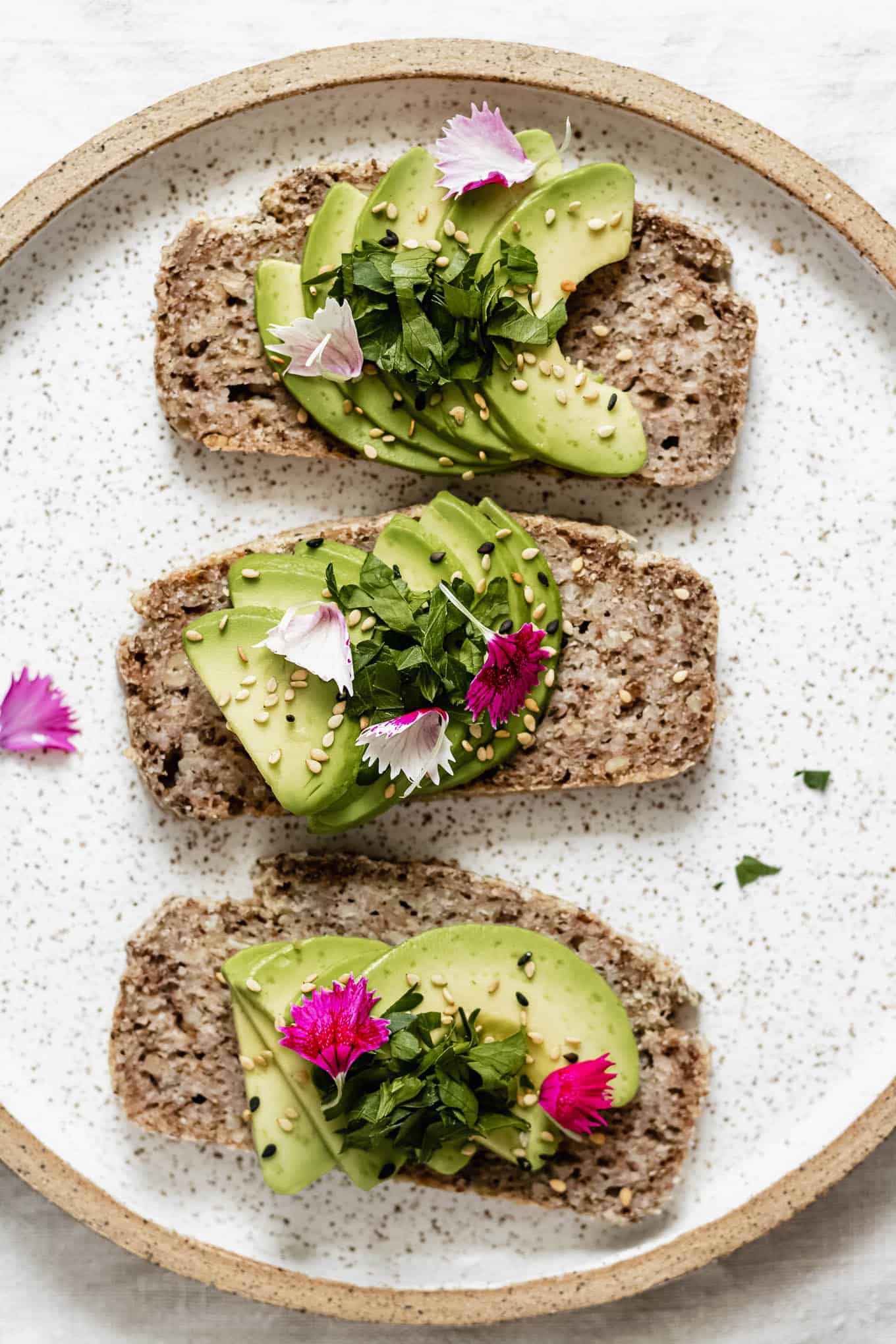 three slices of avocado toast on a plate topped with pink flower petals