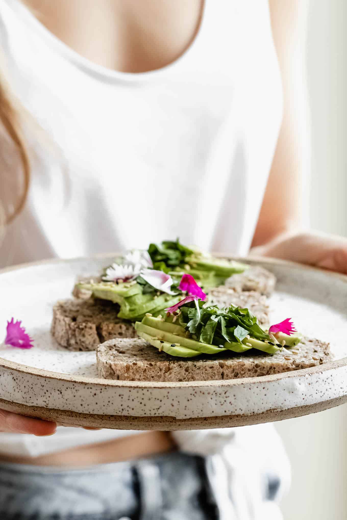 a person holding a white plate with avocado toast on it topped with flower petals