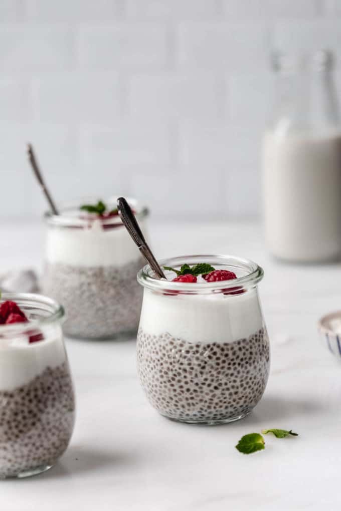 three jars of vanilla chia pudding on a marble countertop with a jar of coconut milk in the back