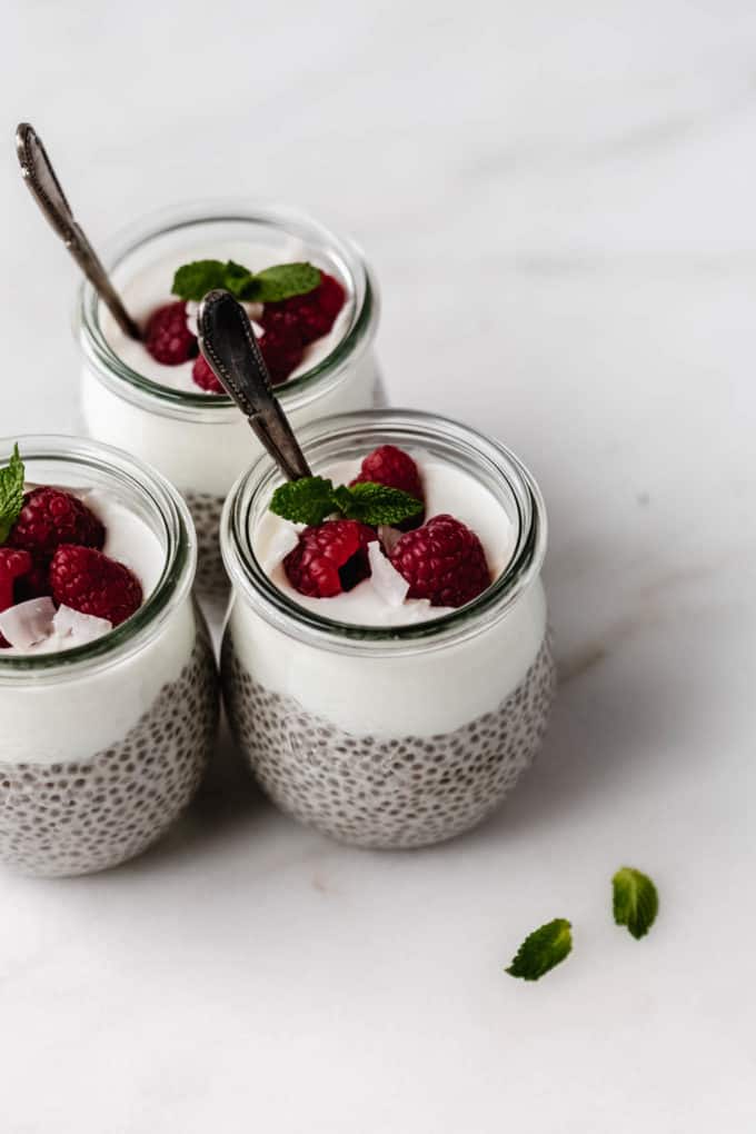three jars of chia pudding with yogurt, raspberries and mint on top