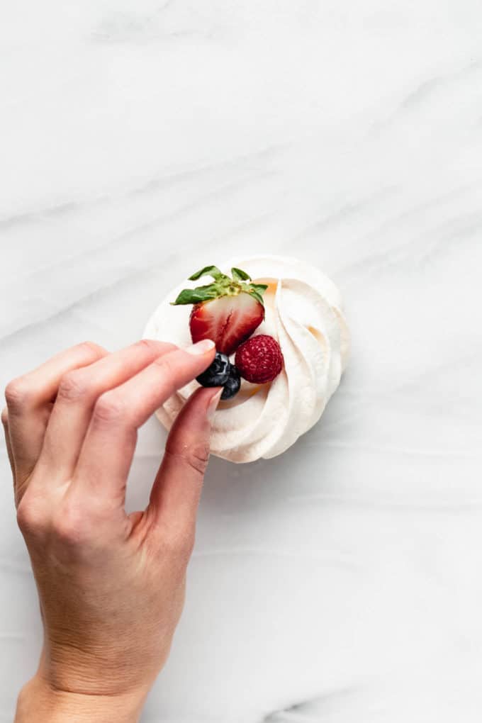 a hand putting blueberries on a pavlova