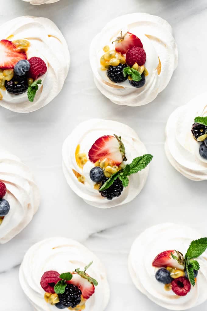 mini pavlovas on a white marble counter topped with fresh fruit and mint leaves