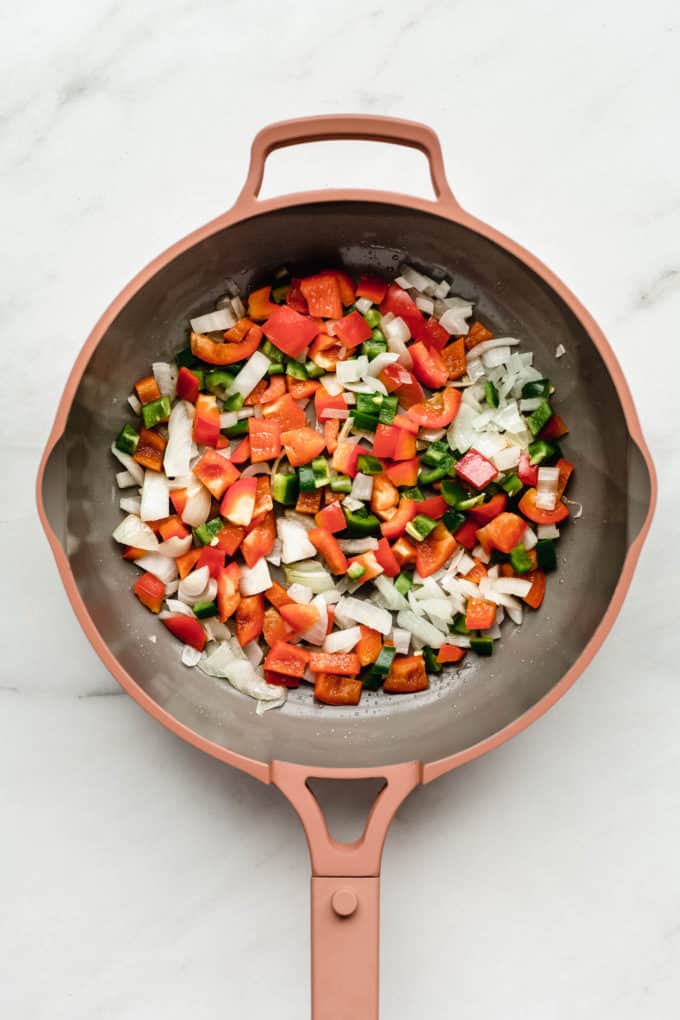 A pink pan with peppers and onions in it