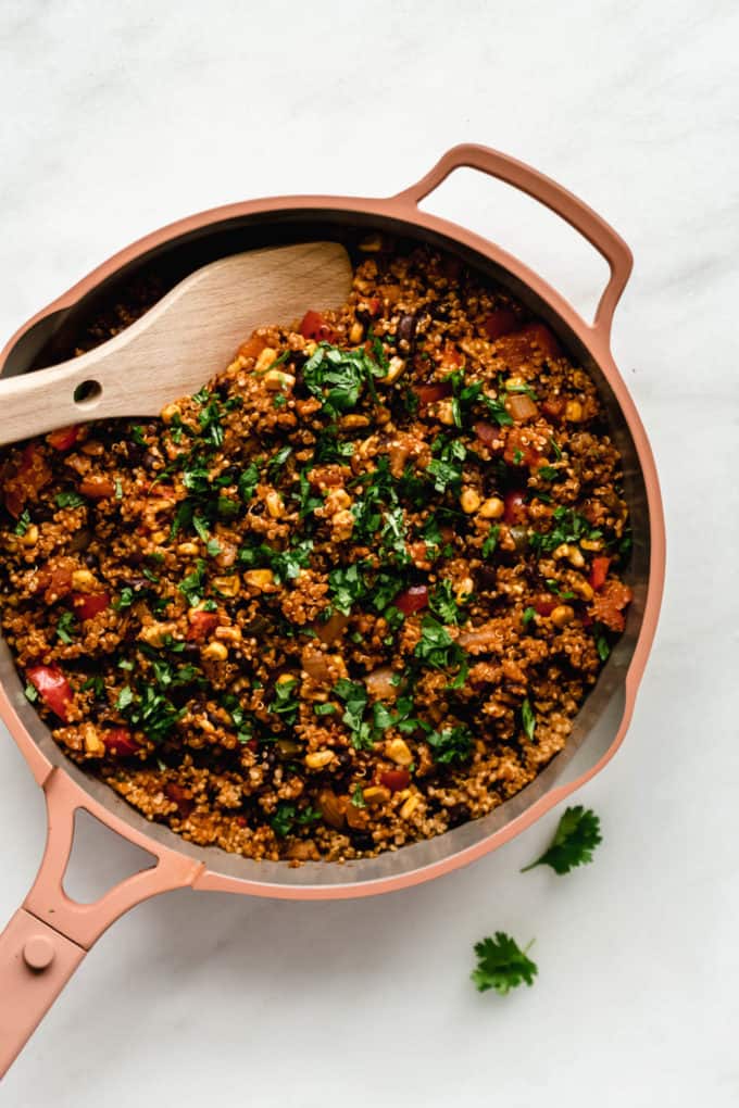 A pan of Mexican quinoa with a wooden spoon in it topped with cilantro