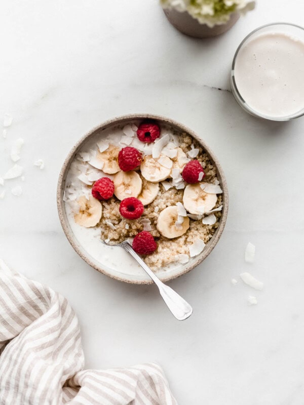 A breakfast quinoa bowl topped with bananas and berries with a glass of milk and flowers on the side