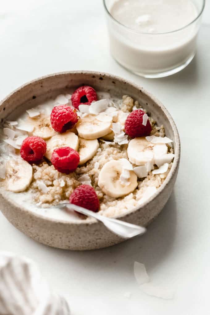a bowl of quinoa topped with banana raspberries and coconut flakes
