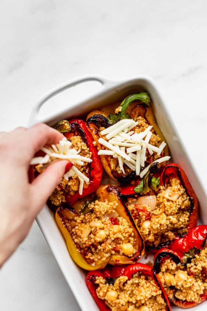 A hand sprinkling shredded cheese onto a baking dish with stuffed peppers
