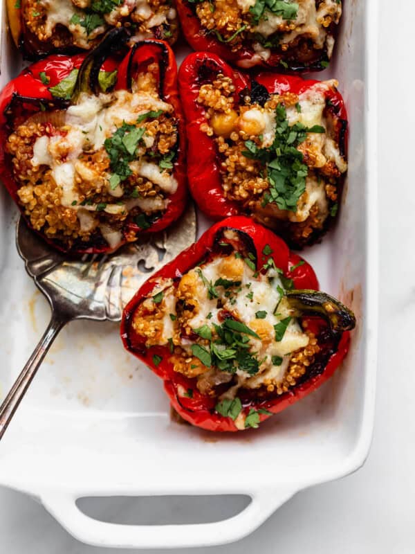 Quinoa stuffed red bell peppers topped with melted cheese in a white baking dish