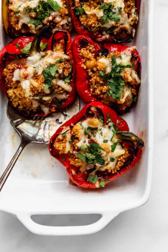 Quinoa stuffed red bell peppers topped with melted cheese in a white baking dish