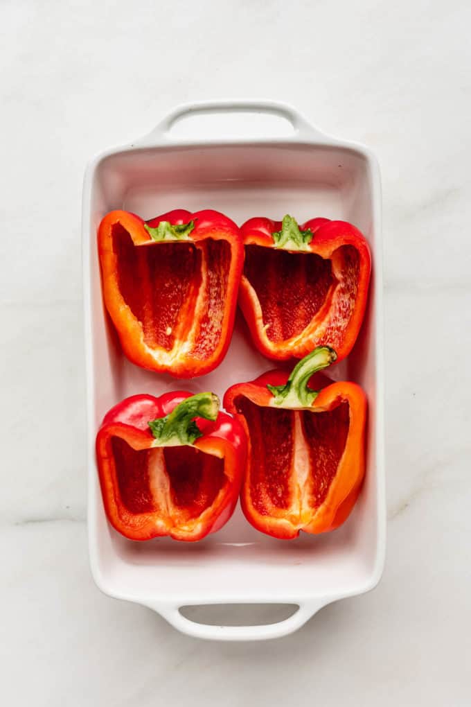 2 red bell peppers slice in half in a white baking dish