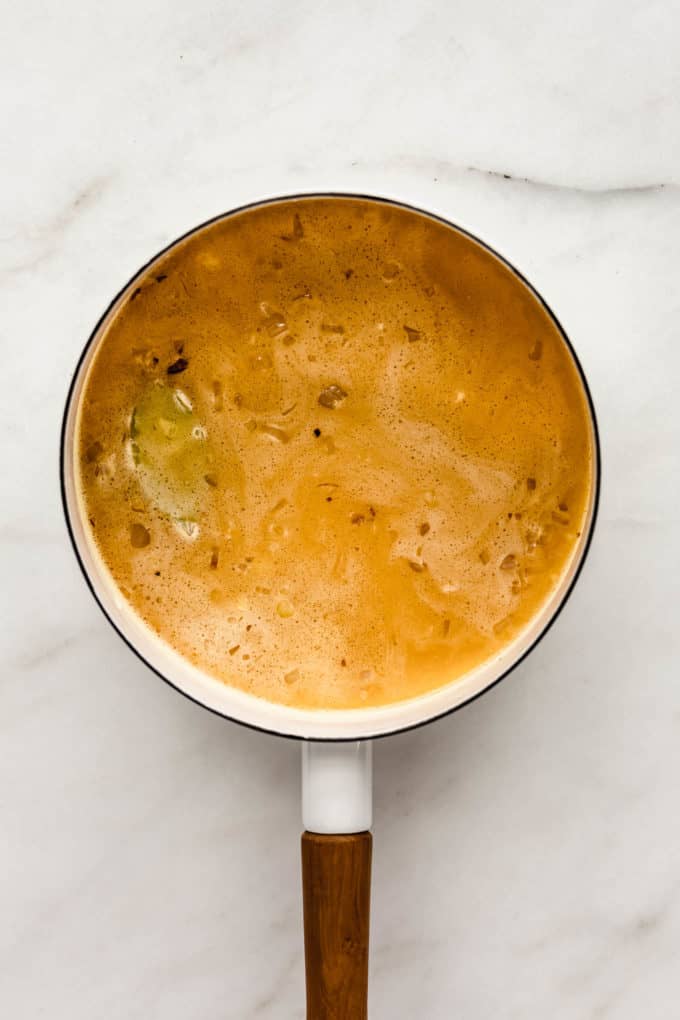 A white pot with rice, veggie stock and turmeric in it