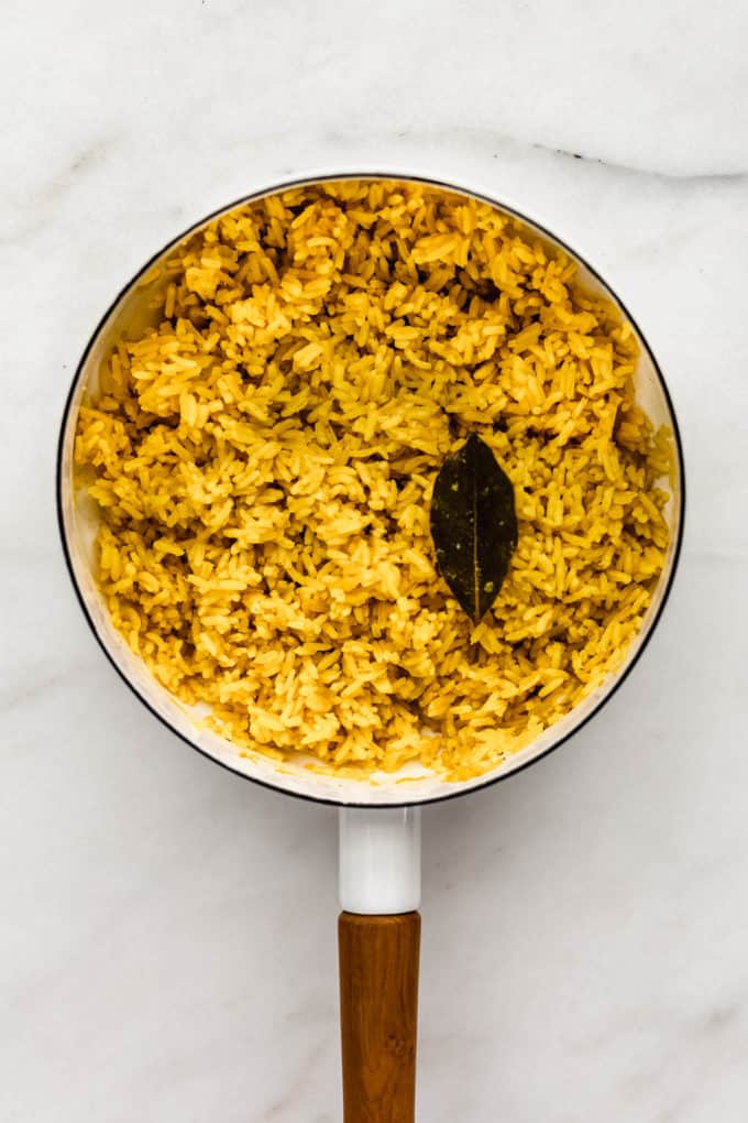 A white pot with turmeric rice and a bay leaf in it