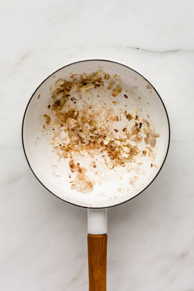 A white pot with sautéed shallots in it