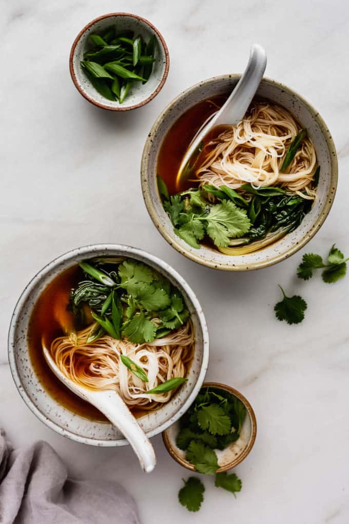 two bowls of pho soup with noodles and bok choy in them