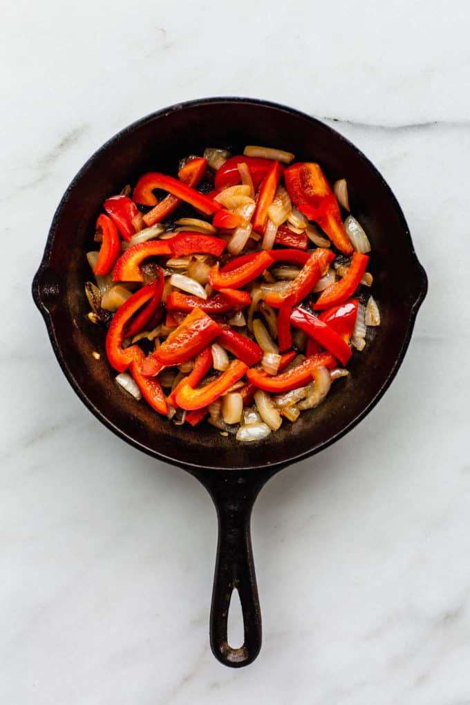 A cast iron skillet with sliced peppers and onions in it