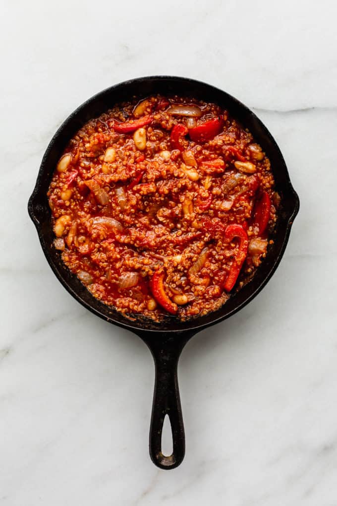 Quinoa, crushed tomatoes, red peppers and white beans in a cast iron skillet
