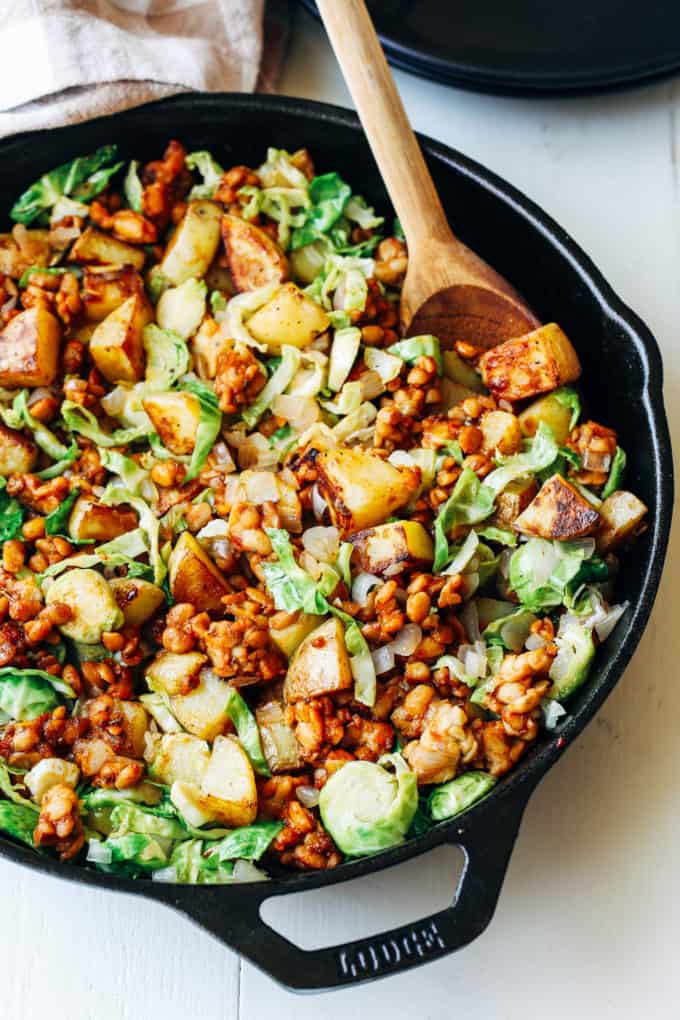 A cast iron skillet with vegetables, potatoes and brussels sprouts in it