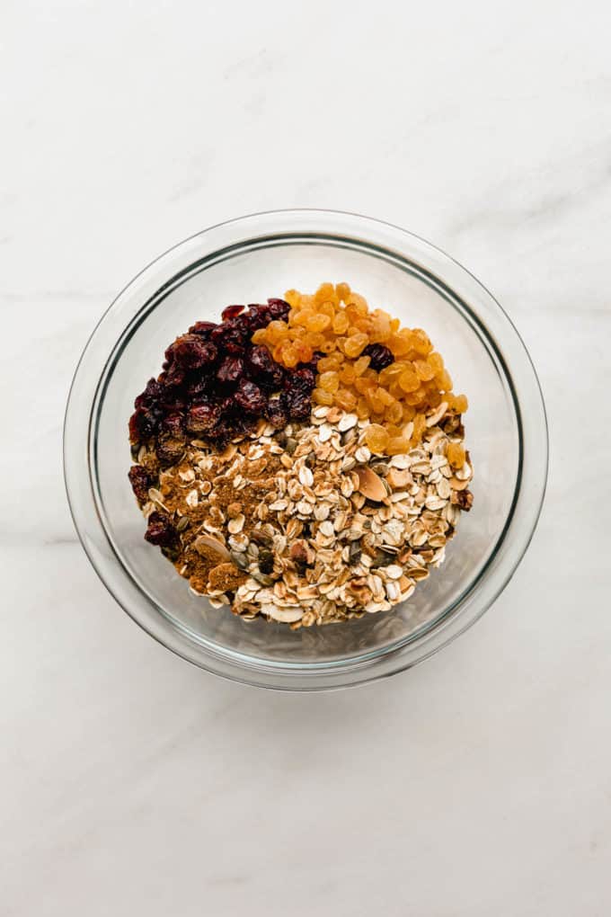 oats, nuts, dried cranberries and golden raisins in a clear mixing bowl