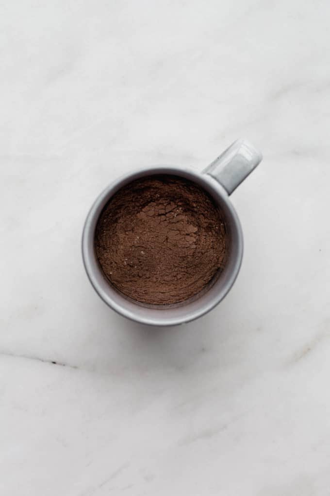 A grey mug with cocoa powder and flour in it