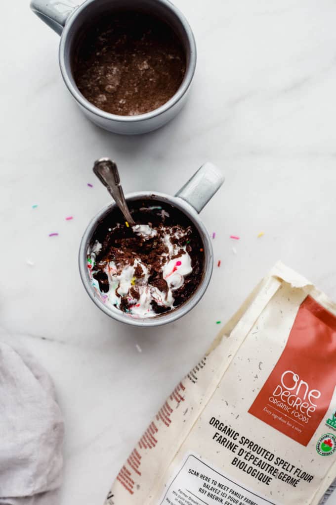a mug filled with cake and whipped cream and a bag one one degree organic spelt flour on the side