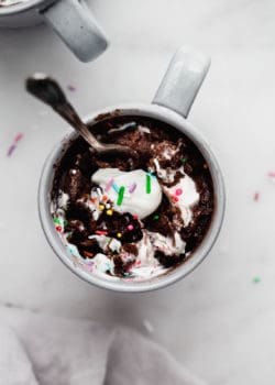 A chocolate mug cake with whipped cream and sprinkles on top