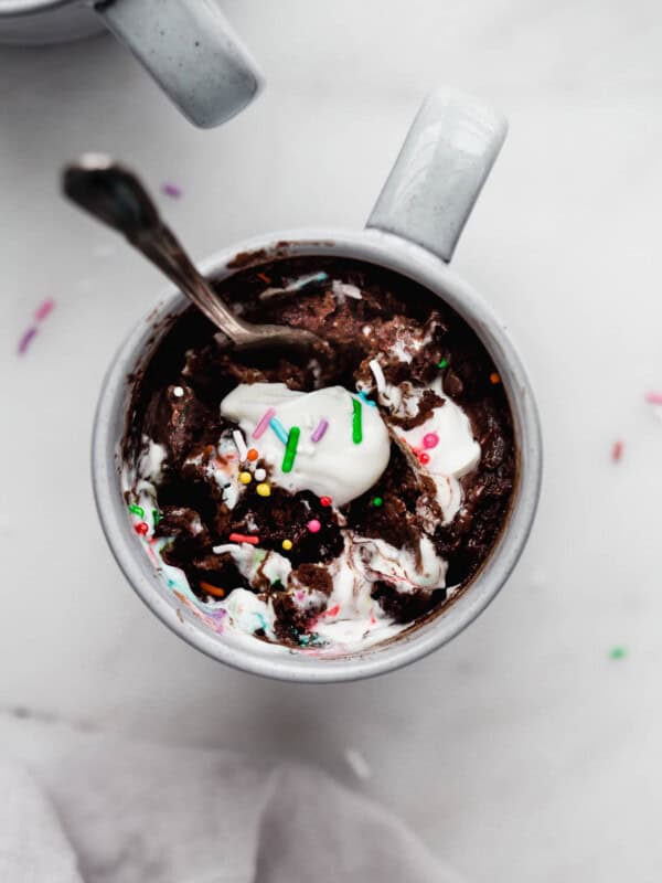 A chocolate mug cake with whipped cream and sprinkles on top