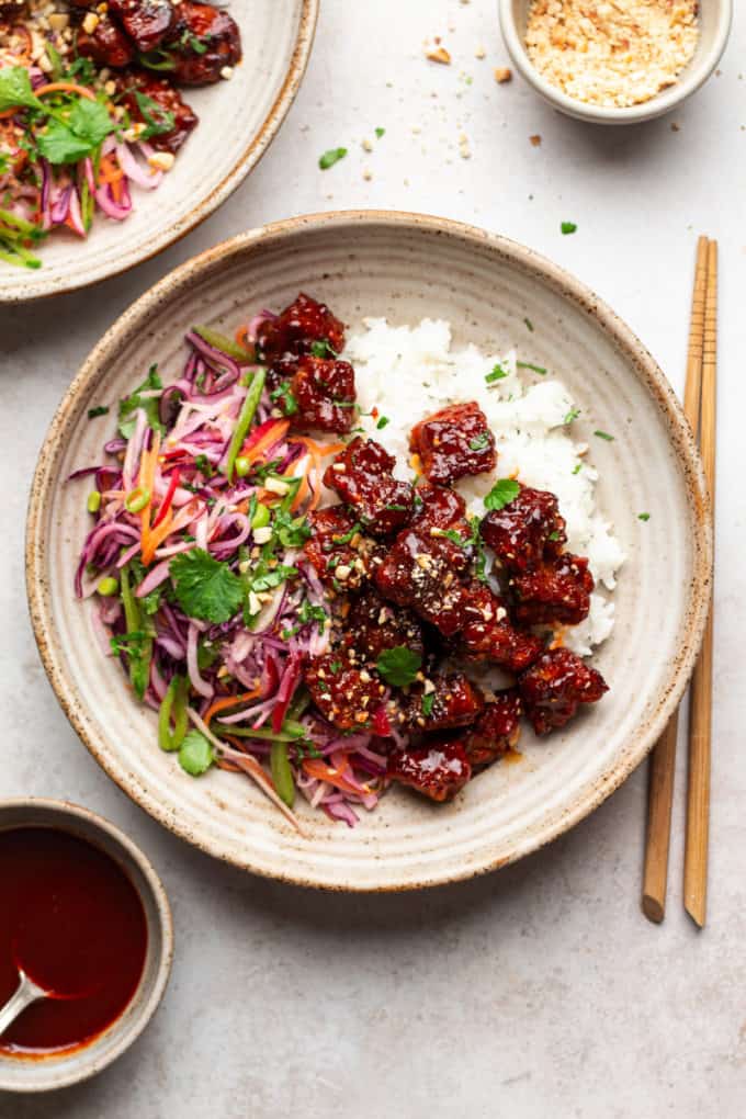 A ceramic plate with rice, slaw and glaze tempeh in it with chopsticks on the side