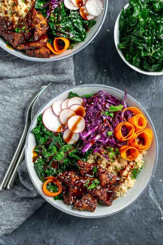 Hoisin glazed tempeh on rice in a white bowl with a grey napkin on the side