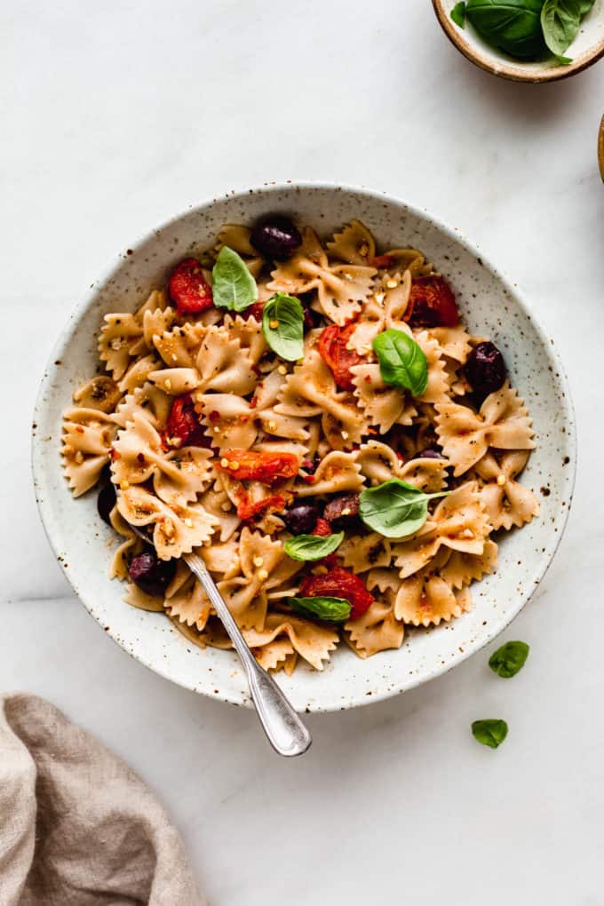 A bowl of mediterranean pasta topped with basil and a napkin on the side