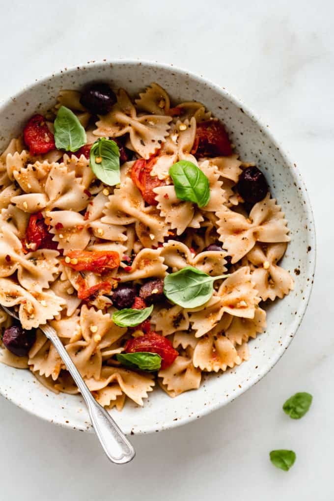 A bowl of farfalle pasta with olives, roasted tomatoes and basil
