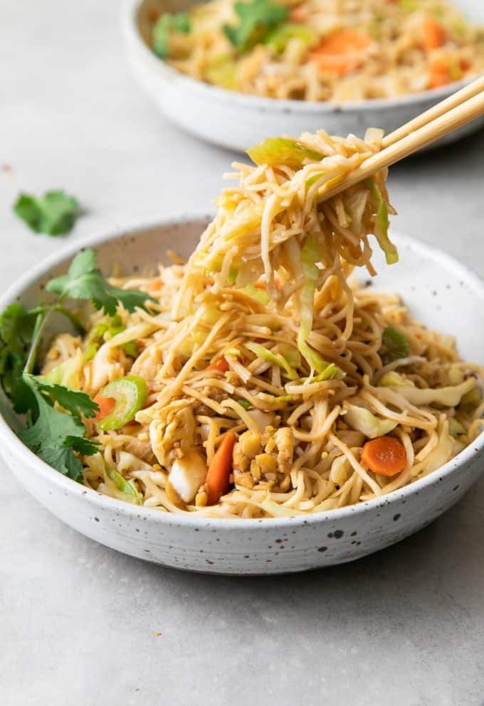 Chopsticks scooping up chow mein from a while bowl